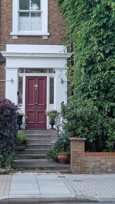 A charming front garden in Wanstead Flats featuring a classic brick townhouse with a white portico entrance and a blue painted door. The entrance is accessed via a short flight of stone steps with whi